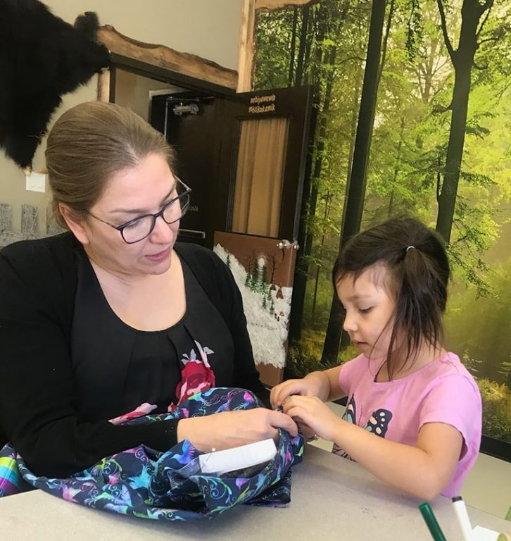 Cultural Studies teacher Janice Clark helps a Kindergarten student master the ribbon skirt sewing technique.